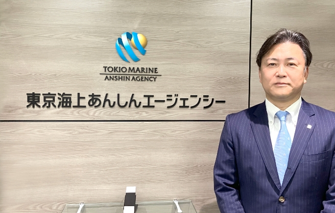 東京海上あんしんエージェンシーのエントランスサインの前に立つ榊田哲也さんの写真