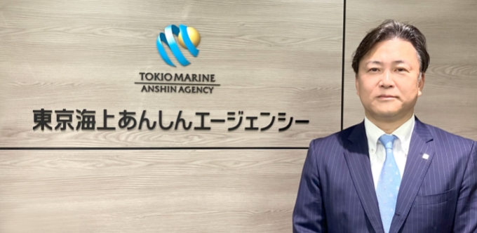 東京海上あんしんエージェンシーのエントランスサインの前に立つ榊田哲也さんの写真